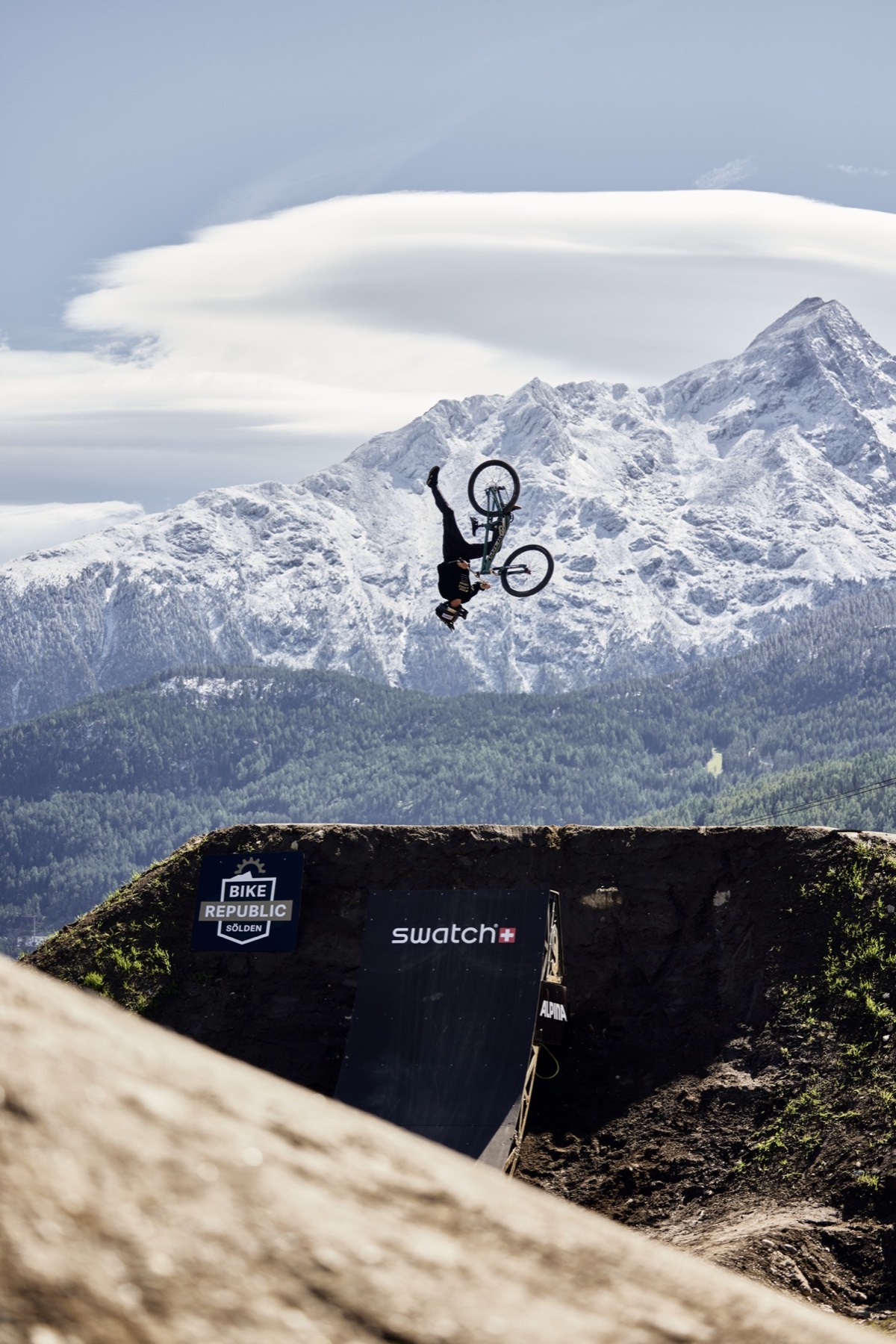 Mountainbiker im Backflip vor verschneiten Bergen