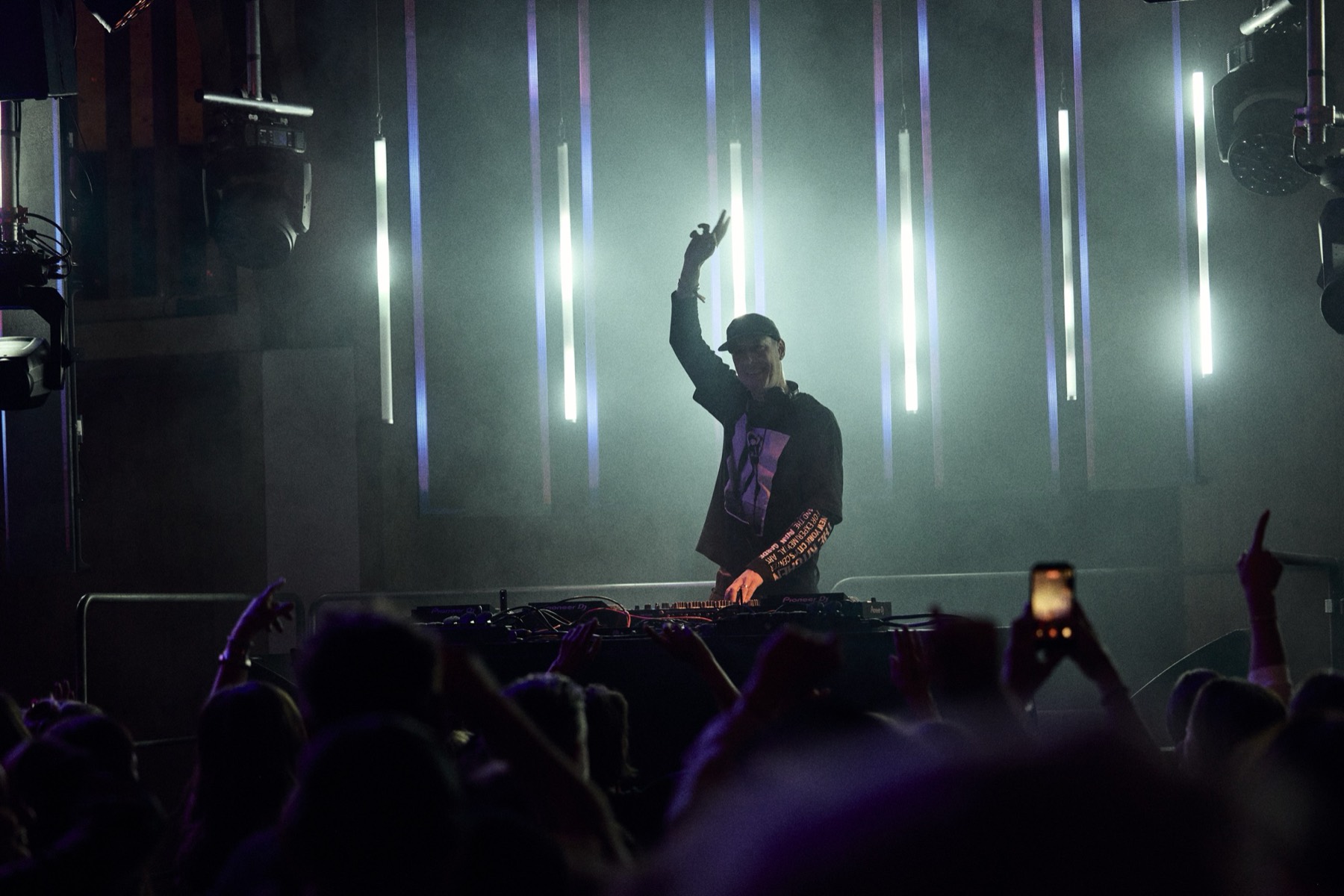 DJ mit erhobenem Arm, das Publikum filmt mit dem Handy