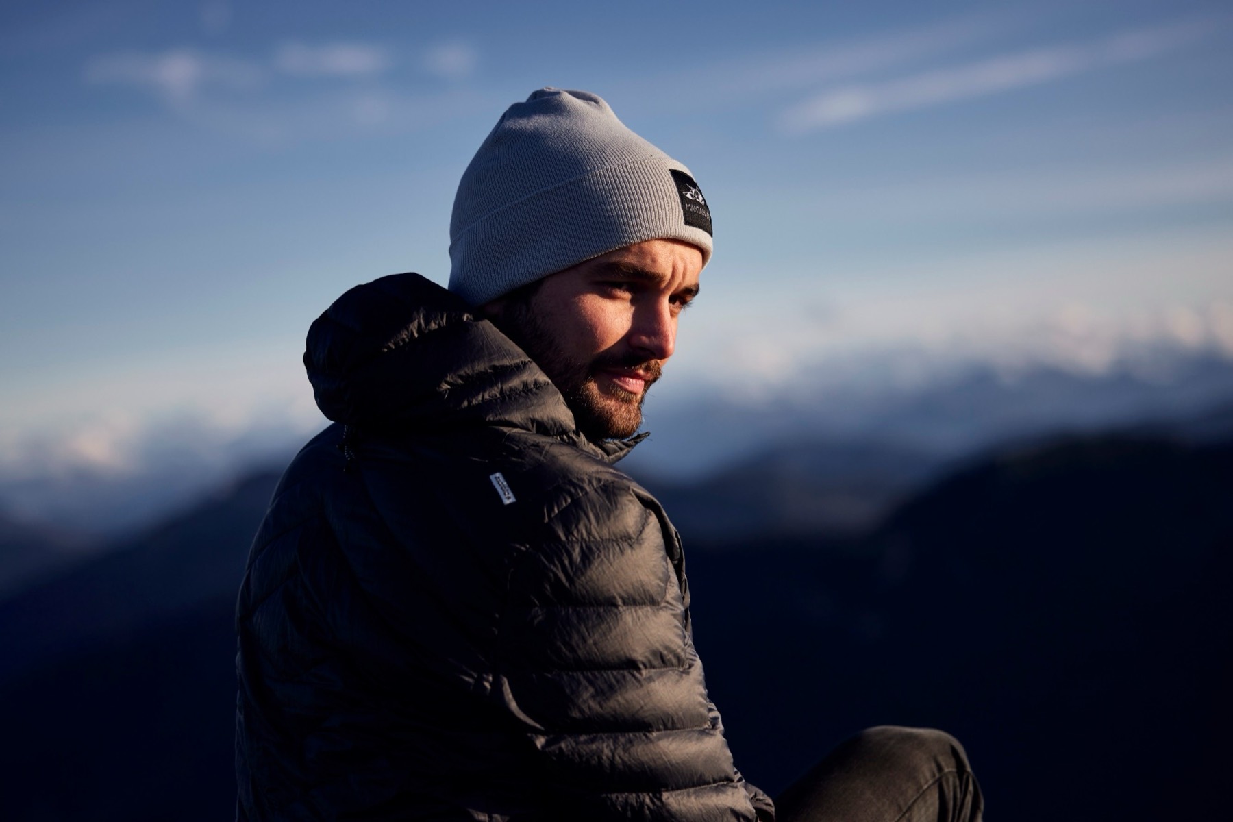 Mann mit Mütze und Daunenjacke vor Bergpanorama