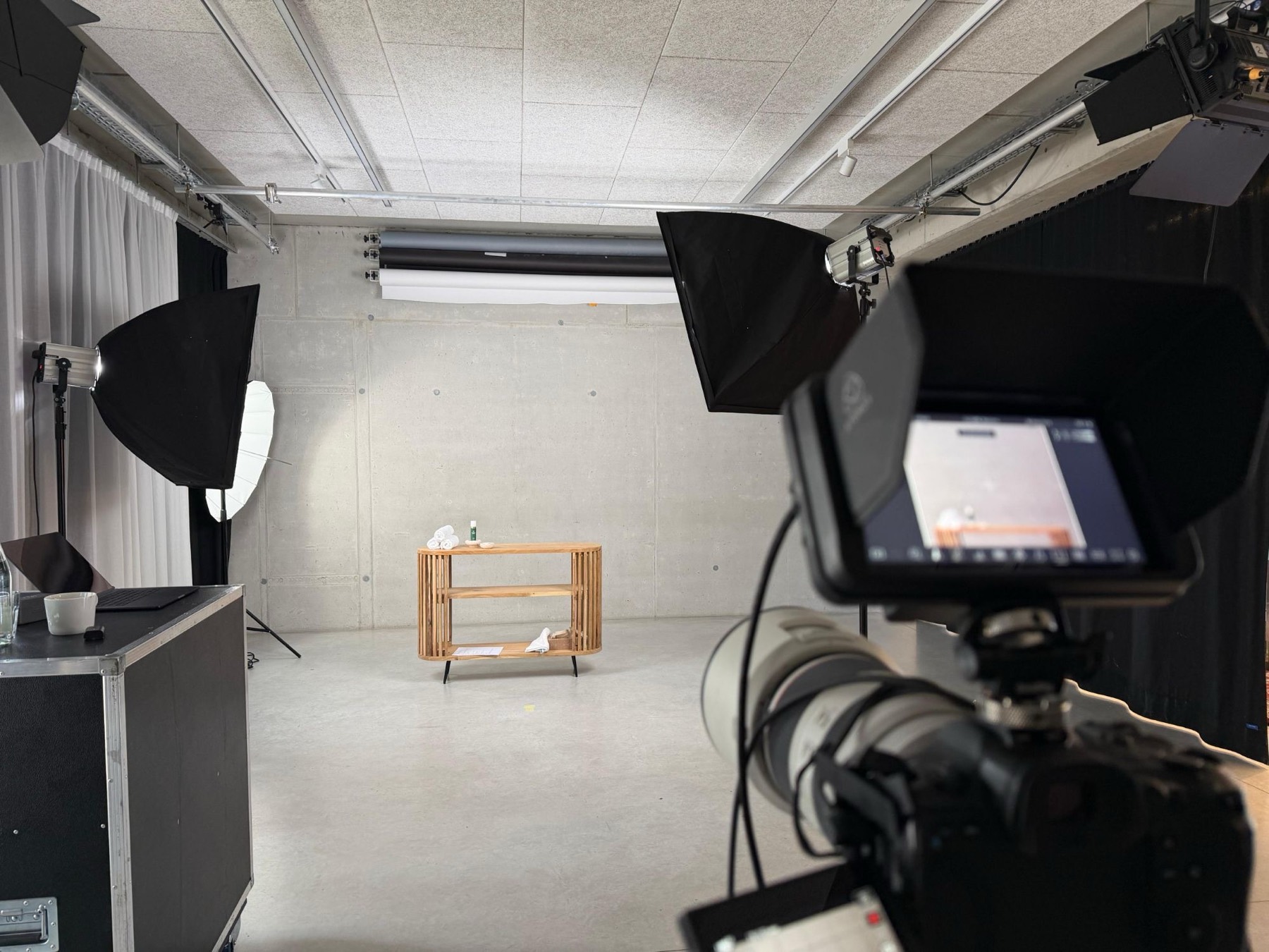 Studio-Set mit Softboxen, Kamera und Monitor, im Hintergrund ein Holzregal als Produktbühne